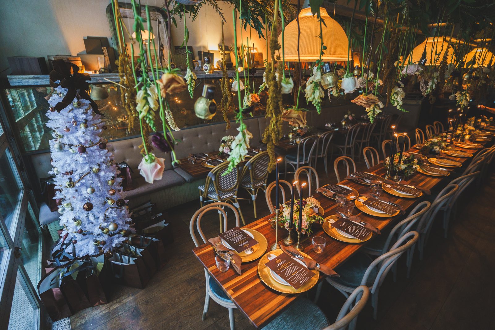 Long holiday dinner table set with gold chargers and a white Christmas tree at an NYC corporate party