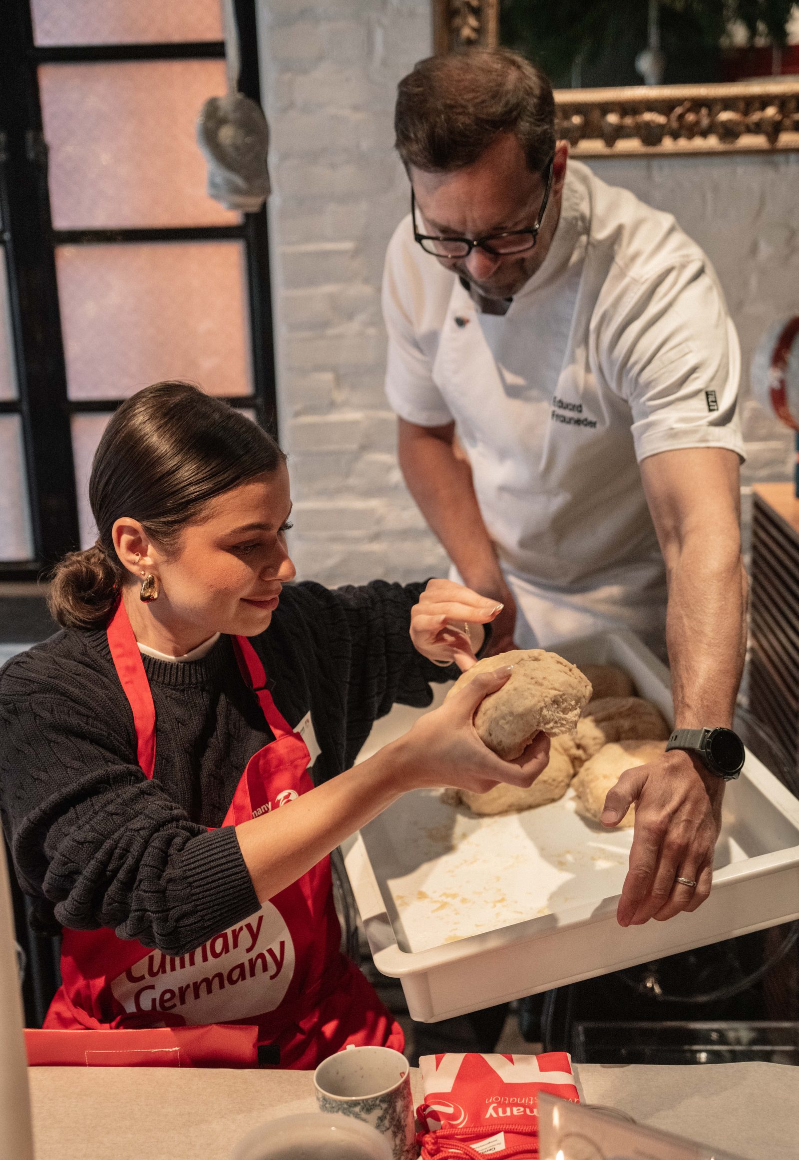 Chef Eduard Frauneder shaping Stollen dough with a guest in a red apron at a corporate holiday baking workshop