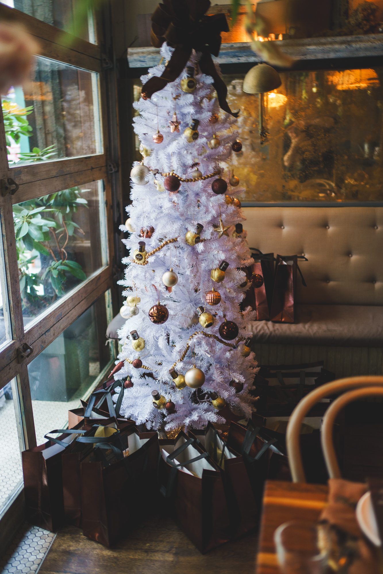 White Christmas tree decorated with chocolate ornaments beside a set holiday dinner table
